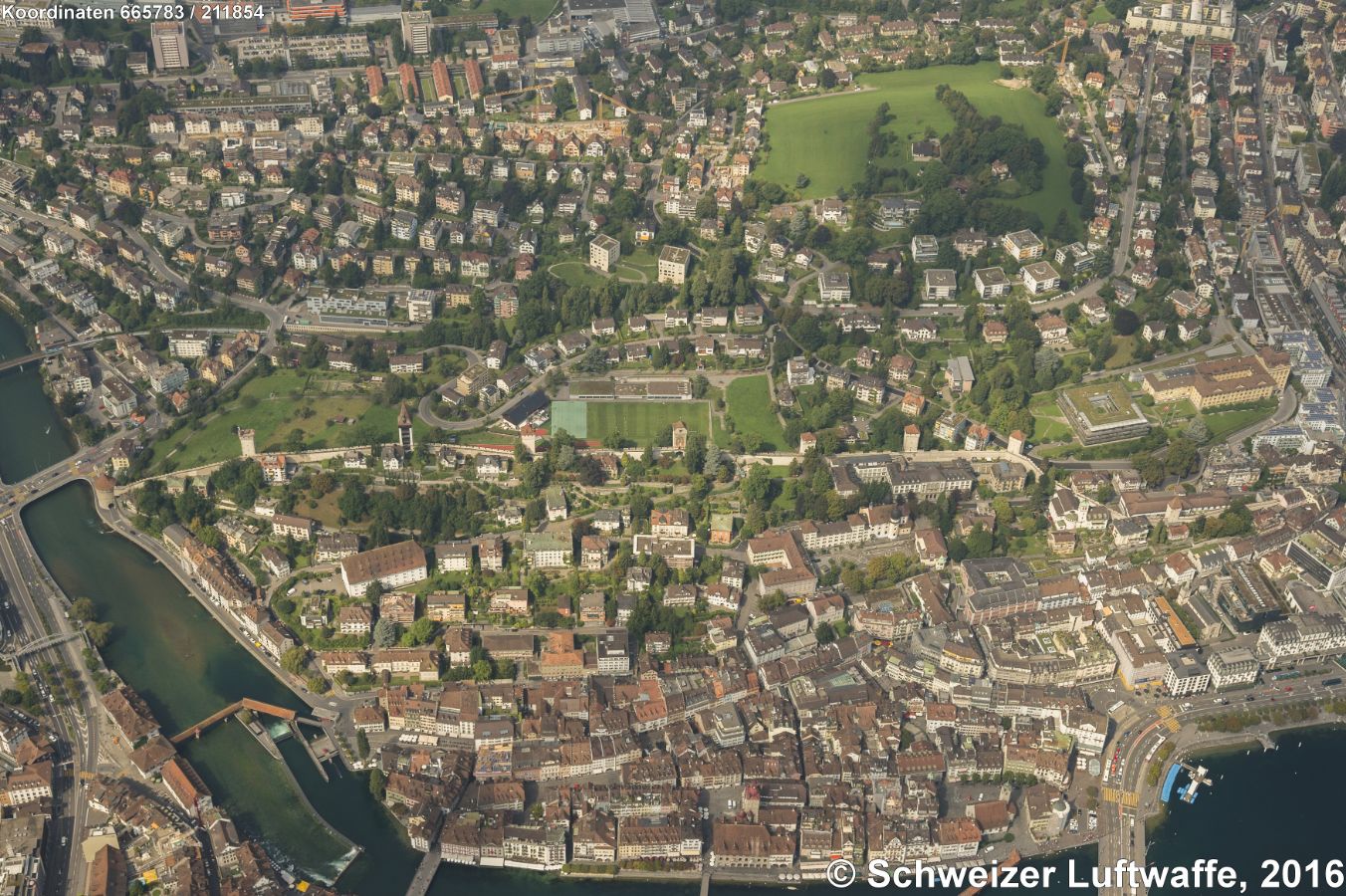 Museggmauer und -türme in der Bildmitte von SW an der Reuss Richtung NE verlaufend. Im Vordergrund die Altstadt West mit der Spreuerbrücke mit Wehr und Kraftwerk. - Bildmitte, etwas rechts: Kantonsschule Musegg (Position 2'665'931.64, 1'211'886.72), davor: Mariahilf-Kirche.